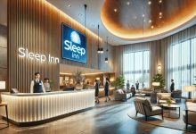 A modern, clean Sleep Inn hotel lobby with bright lighting and stylish furniture, creating a welcoming and cozy atmosphere. The reception desk is staffed by a friendly employee, and guests are either checking in or relaxing in the lobby.