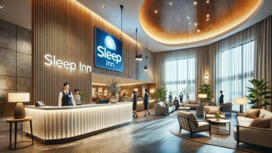 A modern, clean Sleep Inn hotel lobby with bright lighting and stylish furniture, creating a welcoming and cozy atmosphere. The reception desk is staffed by a friendly employee, and guests are either checking in or relaxing in the lobby.